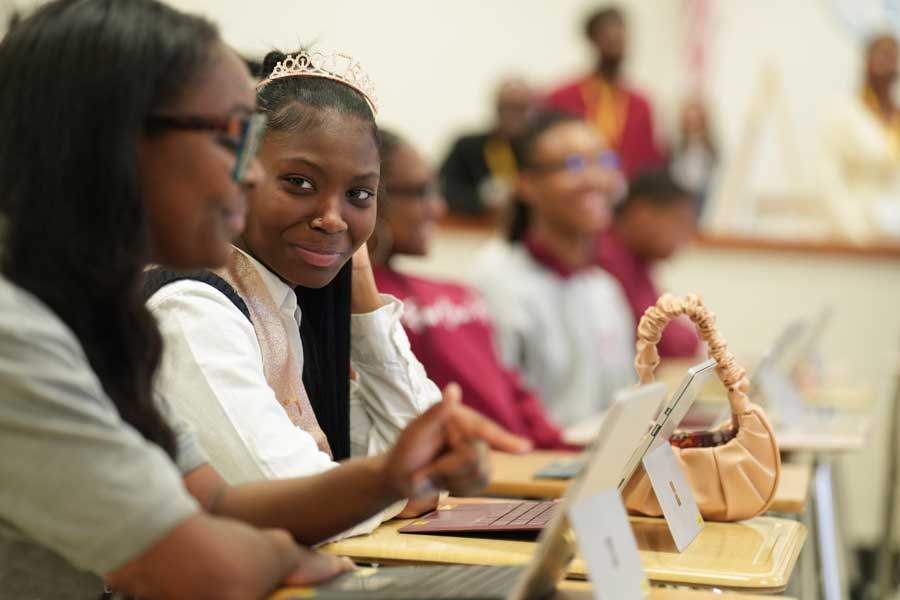 Two young women in a classroom looking at their computers.