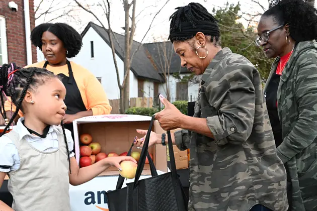 Two men wearing aprons cooking alongside a child wearing a green Ludacris Foundation apron.