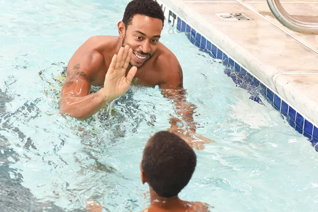 Chris 'Ludacris' Bridges high-fives a youth. They are both swimming in a pool.